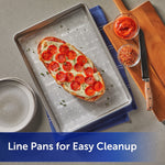 Sheet pan lined with Reynolds Kitchens SmartGrid parchment holding a pepperoni-topped bread on a countertop with utensils nearby