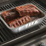Aluminum disposable utility pan on a grill filled with cooked ribs and barbecue sauce