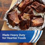 Cooked meat pieces resting on crumpled aluminum foil on a wooden board, highlighting heavy duty foil for heartier foods