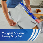 Hands pulling wide sheet of Reynolds Wrap Heavy Duty aluminum foil from box over a cutting board