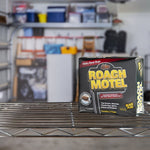 Roach Motel product box placed on a wire shelf with a blurred garage storage background.