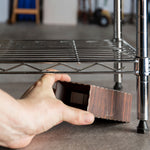 Hand placing a Roach Motel style cardboard trap under a metal shelf in a storage area.