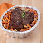 Seared roast beef with carrots and potatoes served in an aluminum oval roaster pan on a wooden table