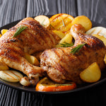 Plated roasted chicken legs with potato wedges, onion slices and rosemary on a dark serving plate