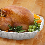 Cooked roasted turkey presented in an aluminum extra-deep oval roaster pan on a wooden surface