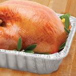 Roasted turkey placed in a disposable extra-deep aluminum pan with garnish on a wood board