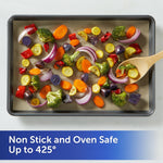 Sheet pan lined with unbleached parchment paper holding roasted mixed vegetables with a wooden spoon