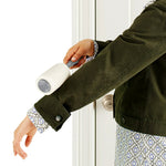 Person rolling a lint roller over the sleeve of a dark jacket to remove lint and pet hair