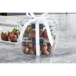 Stacked Rubbermaid Brilliance clear containers tied with a white ribbon, filled with chocolate-covered strawberries and truffles on a marble surface.