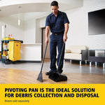 Janitorial worker using a long-handled black upright dustpan and broom on a wood floor in a lobby setting.