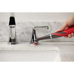 Hand using a red and gray Rubbermaid power scrubber to clean around a chrome faucet on a bathroom sink countertop