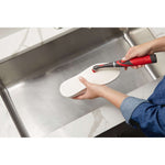 Person using a Rubbermaid power scrubber to clean the surface of a shoe sole over a stainless steel sink