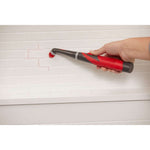 Hand-held Rubbermaid cordless power scrubber being used to clean grout lines on a white subway tile wall