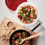 Open Rubbermaid TakeAlongs bowl with red lid nearby, filled with a colorful vegetable and chicken stir-fry on a countertop