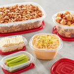 Assortment of clear Rubbermaid containers with red lids holding snacks, dip, crackers and celery on a gray surface