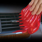 Red cleaning gel being molded into the slats of a car air vent by a hand to remove dust from vents