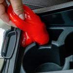 Hand pressing red gel into a car cupholder to pick up dust and debris from tight interior crevice