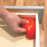 Hand pressing red cleaning gel into the corner of a wooden drawer to lift dust and debris from the edge