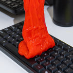 Red cleaning gel being pressed into and lifted from a black computer keyboard to remove dust from keys