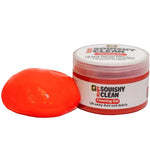 Clear jar of Ruby Squishy Clean red cleaning gel with a portion of the gel sitting beside the container on a white background