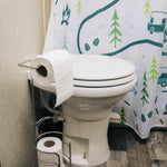 toilet with a roll of white toilet paper on a side holder and extra rolls in a floor stand next to a patterned shower curtain