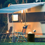 Outdoor RV campsite scene showing folding chairs, table, lantern and a green collapsible trash can beside the RV