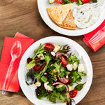 Top-down lifestyle scene with salad plates and clear plastic fork and spoon placed on red napkins
