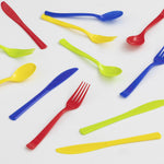 Scattered multicolor disposable plastic forks, spoons and knives on a white background