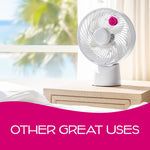 Small pink circular scent disc clipped to a white desk fan placed on a bedside table with a blurred window view