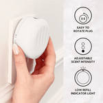 Hand rotating a white Scent Theory plug-in diffuser mounted in a wall outlet with feature icons on the right