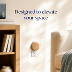 Lifestyle scene of a wood-finish Scent Theory plug-in diffuser in a living room outlet beside shelving and a sofa