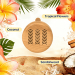 Woodgrain circular car vent diffuser surrounded by tropical flowers, coconut and sandalwood labels on sandy background
