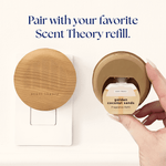Top-down view of wood-finish Scent Theory plug-in diffuser mounted in outlet next to a hand holding a Golden Coconut Sands refill
