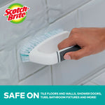 Scotch-Brite scrub brush being used on tiled grout, showing white and teal bristles in use