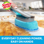 Scotch-Brite dishwand scrubbing a baked-on mess on a flat pan surface with suds and brand logo overlay.
