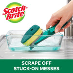 Scotch-Brite dishwand being used to scrape and scrub a glass dish with soap suds in a sink