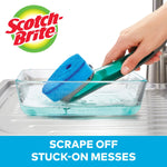 Hand using a Scotch-Brite dishwand to scrub inside a glass dish filled with soapy water, brand logo visible.