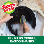 Two hands using a Scotch-Brite dishwand to wash a large black plate in a sudsy kitchen sink