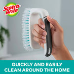 Hand holding a white Scotch-Brite scrub brush with teal-accented bristles and brand logo