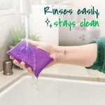 Hand holding a purple Scotch-Brite scrubbing pad under running faucet water with text 'Rinses easily, stays clean'.