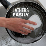 Hand using a white Scotch-Brite Greener Clean scrub pad to lather and clean the interior of a nonstick skillet over a sink