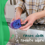 Hands rinsing a Scotch-Brite dishwand refill under running faucet, text noting it 'rinses clean + resists odors'