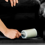 Hand using a Scotch-Brite lint roller under a dark couch cushion to remove debris from upholstery.