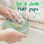 Person scrubbing a bowl with a floral-patterned pop-up sponge producing suds, with text about a clean that pops.
