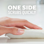Close-up of a hand pressing the textured scrub side of a white Scotch-Brite Greener Clean pad on a countertop
