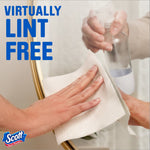 Person wiping a mirror with a Scott paper towel, labeled 'Virtually lint free' in large blue text