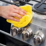 Hand cleaning stainless steel stove knob with a bright yellow Scrub Daddy microfiber cloth