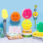 Bathroom countertop scene with assorted Scrub Daddy smiley sponges, cleaning paste tubs and tools arranged against a blue wall