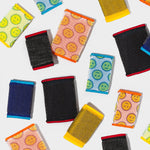 Flat lay of assorted Scrub Daddy Scour Daddy mesh scouring pads scattered on a white surface showing different colors and textures