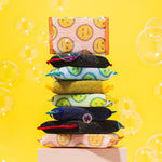 Stacked colorful Scrub Daddy scouring pads and sponges on a yellow background with soap bubbles for a playful lifestyle shot